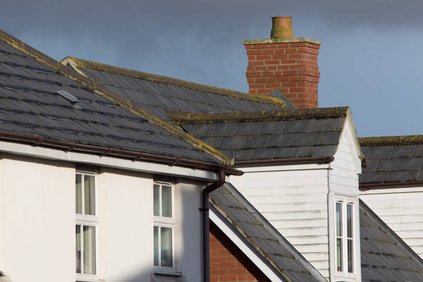 Modern town house roof with slate tiles, chimney and white dormer window Modern town house roof with slate tiles, chimney and dormer with white pvc window and wood cladding. Brown guttering. slate ridge stock pictures, royalty-free photos & images