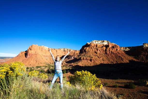Wilderness Victory: Woman with Arms Raised in Joy Wilderness victory: Senior Woman in early morning with arms raised in joy in front of red-orange rocks. Shot in Abiquiu, 50 miles north of Santa Fe, NM. Copy space in the vibrant blue sky. rabbit brush stock pictures, royalty-free photos & images