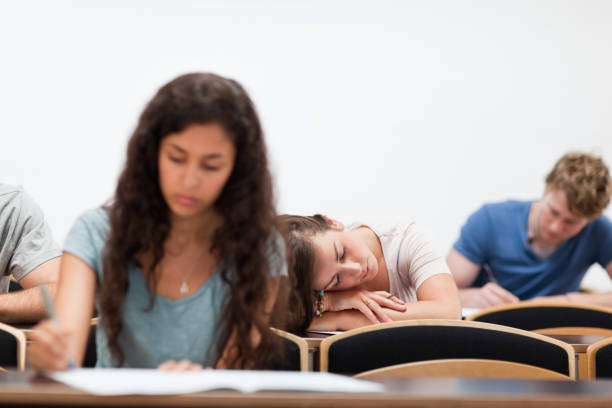 Students working while their classmate is sleeping Students working while their classmate is sleeping in an amphitheater male college student sleeping through lecture stock pictures, royalty-free photos & images