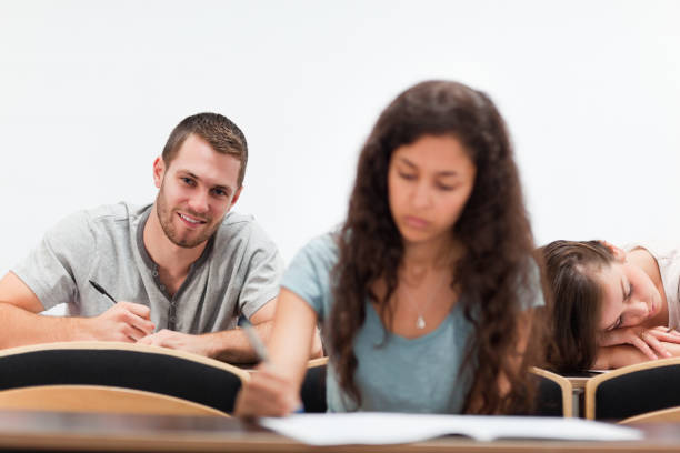 Smiling students writing while their classmate is sleeping Smiling students writing while their classmate is sleeping in an amphitheater male college student sleeping through lecture stock pictures, royalty-free photos & images