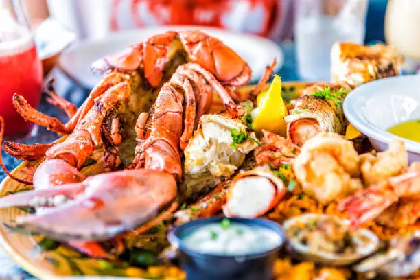 Macro closeup of red lobsters, shrimp, crab, oyster and seafood platter on plate in restaurant with tartar sauce