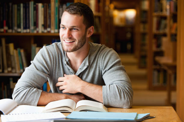 Smiling male student working Smiling male student working in a library adult education book stock pictures, royalty-free photos & images