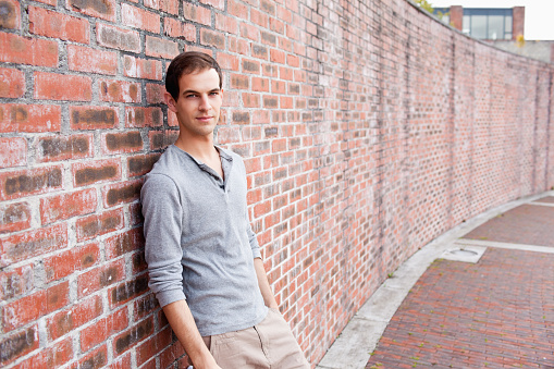 Male student leaning on a wall outside a building