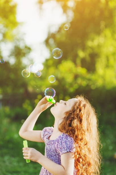 istock Curly girl blowing soap bubbles in summer park. 855709400