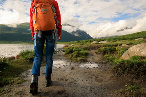 A hiker walks along a leaf-covered path in a vibrant autumn forest wearing a bright yellow raincoat and sturdy boots. Healthy lifestyle on leisure activity