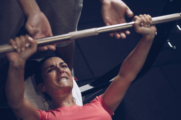 zdeterminowana zawodniczka podejmując wysiłek podczas wykonywania ćwiczeń wyciskania ławki z trenerem. - women weight bench exercising weightlifting zdjęcia i obrazy z banku zdjęć