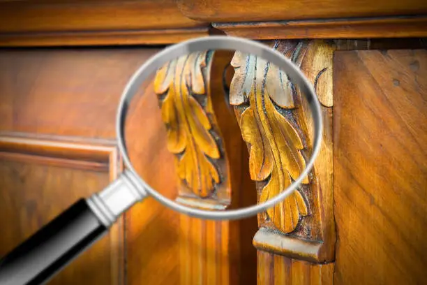 Photo of Detail of an antique wooden italian furniture just restored with a magnifying glass on foreground looking for woodworm threat detection