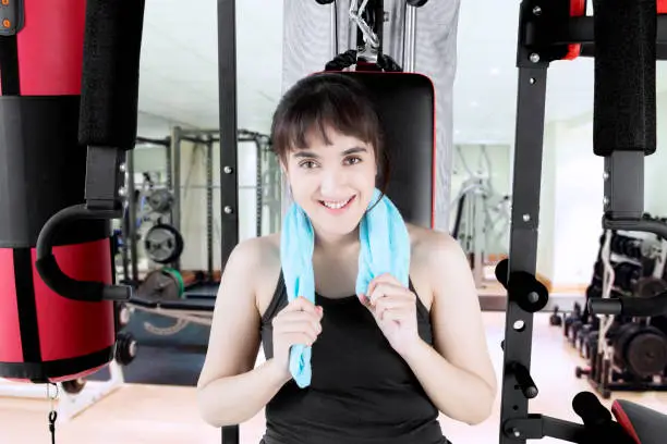 Arabian woman sitting on the gym equipment after doing exercise while smiling at the camera