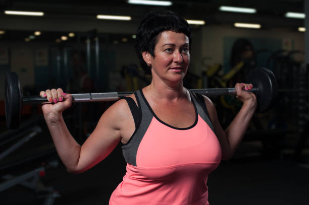 istock Middle aged woman exercising with barbell in gym 855779548