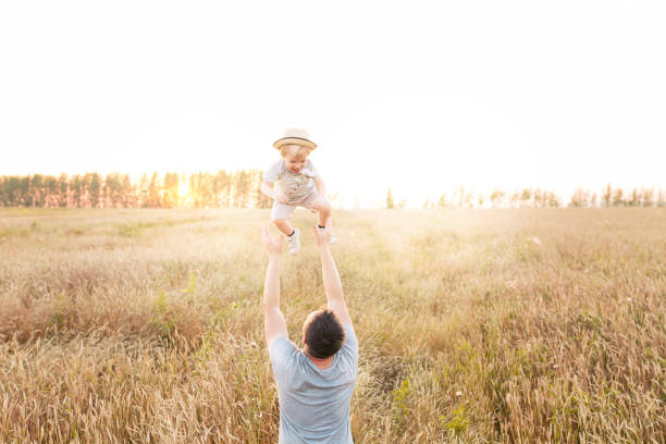 Father and son playing in the wheat field at the sunset time. Dad with kid having fun on the field. Concept of friendly family and of summer vacation. stock photo
