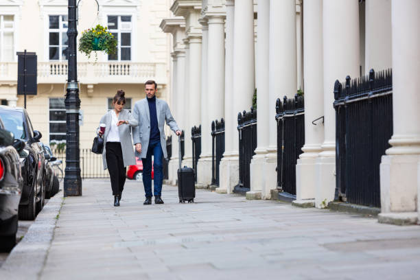 Elegant couple walking in the city street, man carrying suitcase Business travel. Smart casual couple walking in the city street, woman holding take away coffee, man carrying suitcase. Autumn season. victoria house stock pictures, royalty-free photos & images