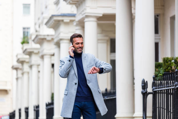 Handsome elegant man walking the city street and talking on phone Elegant handsome man walking the city street, talking on phone and checking time. Autumn season. victoria house stock pictures, royalty-free photos & images