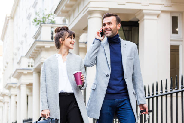 Elegant couple walking in the city street, man talking on phone Happy, legant couple walking in the city street, woman holding take away coffee, man talking on mobile phone. Autumn season. victoria house stock pictures, royalty-free photos & images