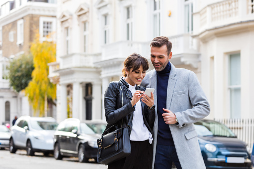 Elegant couple using smart phone together in the city street in London. Autumn season.