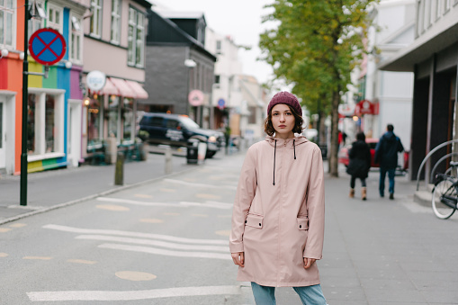 Young Caucasian woman  in pink raincoat walking in ​ Reykjavik