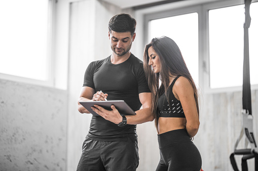 Fitness instructor show the young woman her exercise plan on the digital tablet
