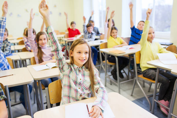 istock group of school kids raising hands in classroom 855812492