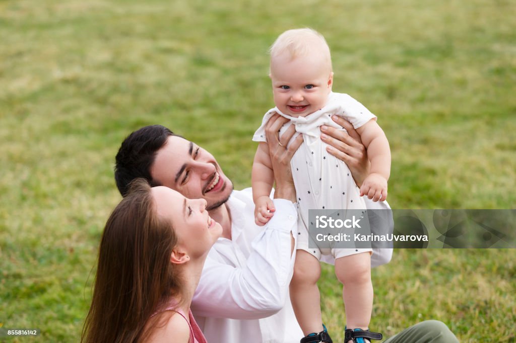 Happiness and harmony family life concept. Young mother and father with baby son in the park. Happy family resting together on the green grass Happiness and harmony family life concept. Young mother and father with baby son in the park. Happy family resting together on the green grass at summer Adult Stock Photo