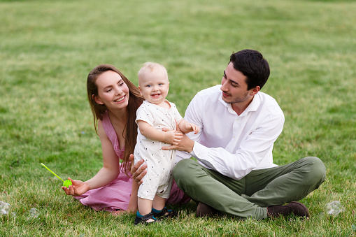 Happy young family with baby boy spending time together outside in green nature at summer