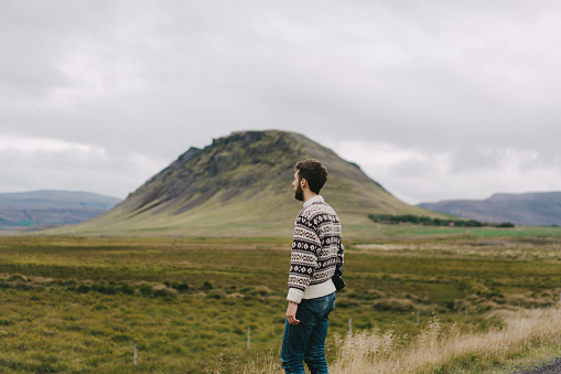 Young Caucasian man in sweater looking at scenic landscape of mountains in Iceland