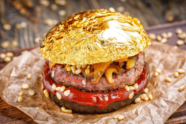 gold beef burger with a black bun,with arugula and cheese and ketchup sprinkled with pine nuts served on pieces of brown paper on a rustic wooden table, on a dark background. delicious gold burger - beer hamburger american culture beef imagens e fotografias de stock