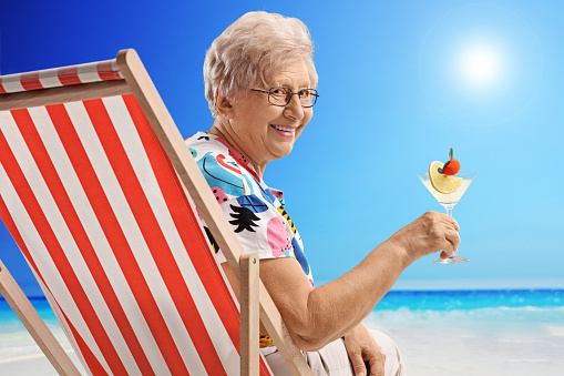 Elderly woman with a cocktail sitting in a deck chair on a beach