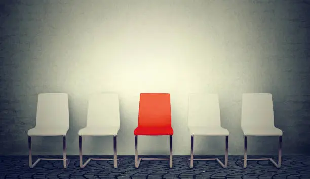 Photo of One opening for the job business concept. Row of white chairs and one red in the middle