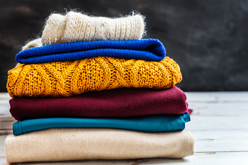 Stack of colorful warm autumn and winter clothes on dark background