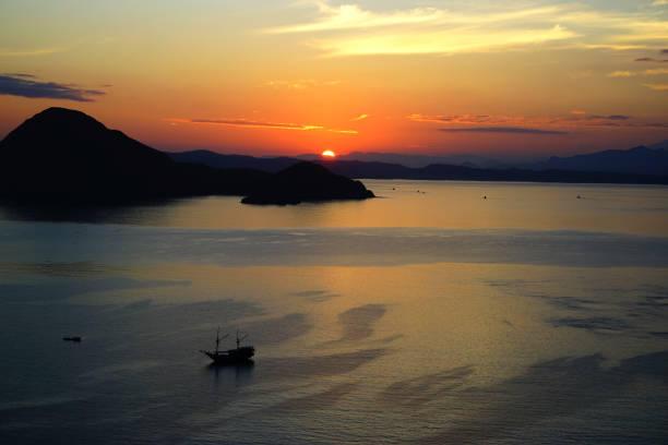 Orange sunrise view from Padar Island part of komodo national park with little silhouette boat in the ocean, Flores Indonesia.