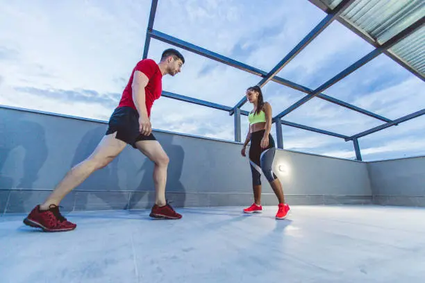 Young woman doing squatson on the roof top with her fitness instructor