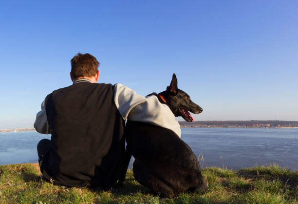 Rear view of a man and dog sitting on beach. man holding his loyal dog