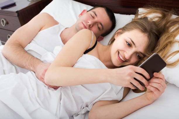 istock girl chatting with mobile, man sleeping by in bed 855894672