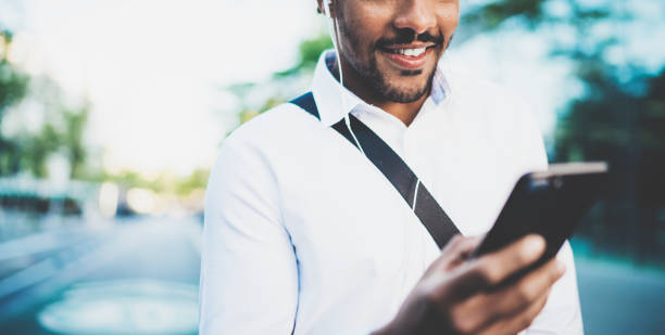 istock Portrait of young smiling african man using smartphone hands while standing at sunny city street.Concept of happy business people working outside.Blurred background.Cropped horizontal. 855910456