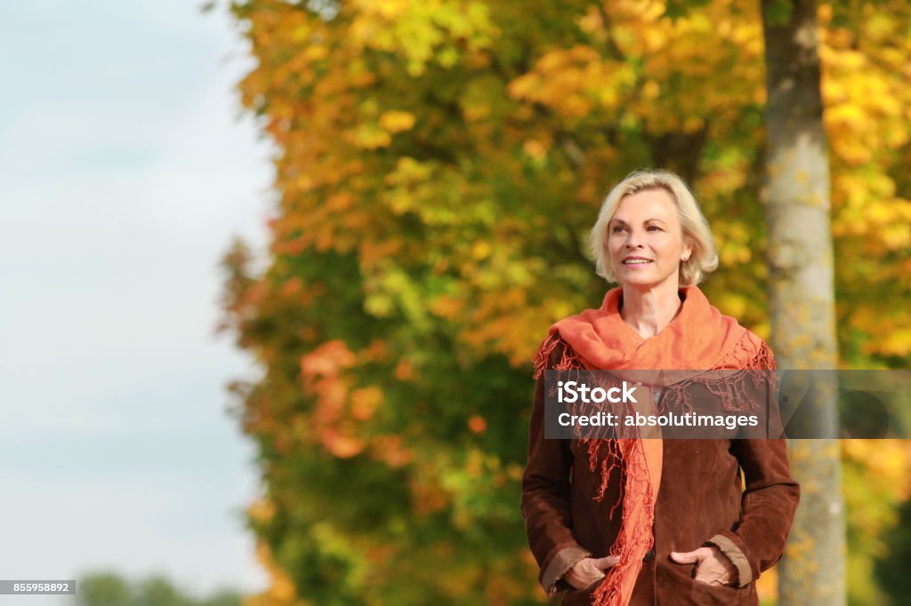 Happy mature woman walks in front of golden autumn leaves Happy mature woman in front of golden autumn leaves enjoys leisure time Mature Women Stock Photo
