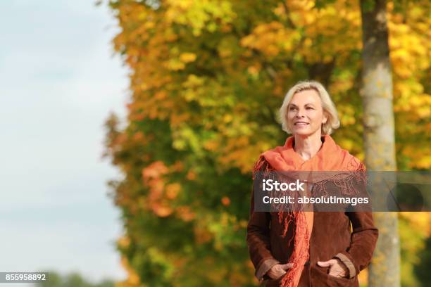 Happy Mature Woman Walks In Front Of Golden Autumn Leaves Stock Photo - Download Image Now