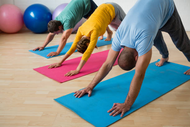 instructor guiding students in practicing downward facing dog pose at yoga studio - concentration flexibility full length healthy lifestyle imagens e fotografias de stock