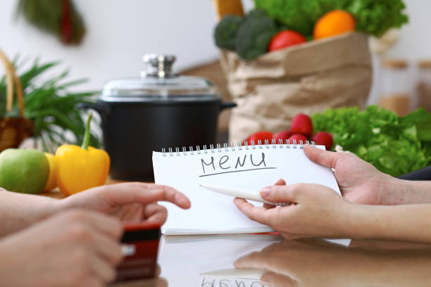istock Close-up of human hands pointing into note book copy space area in the kitchen.  So much ideas for tasty cooking. Vegetarian, healthy meal and friendship concept 855969610