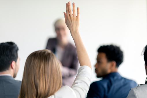 A businesswoman raising a hand to ask the presenter a question at a business meeting in the board room