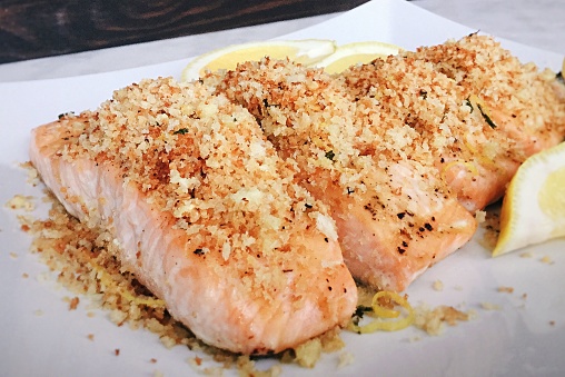 Baled salmon fillet covered with herbed panko breadcrumbs and shown on a white plate with a slice of lemon.