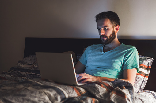 Young man working late in bed on a laptop