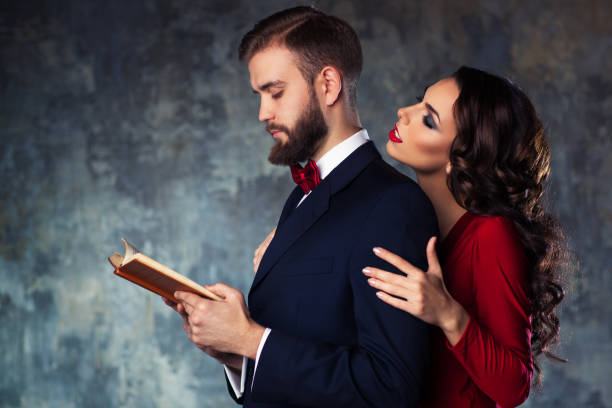 Young elegant couple Young elegant couple in evening dress portrait. Man reading book and woman trying to attract and embrace him. seduction stock pictures, royalty-free photos & images