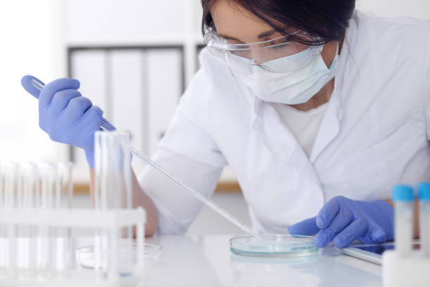 close-up of professional female scientist in protective eyeglasses making experiment with reagents in laboratory. medicine and research concept - medical exam science research scientific experiment imagens e fotografias de stock