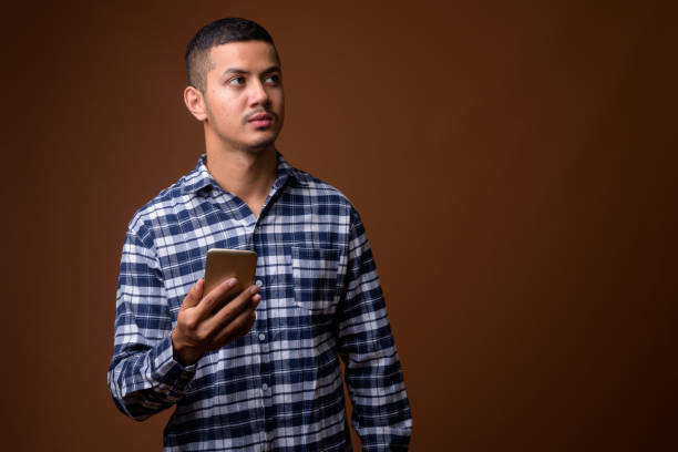 istock Studio shot of young multi-ethnic Asian man using mobile phone against colored background 855993588
