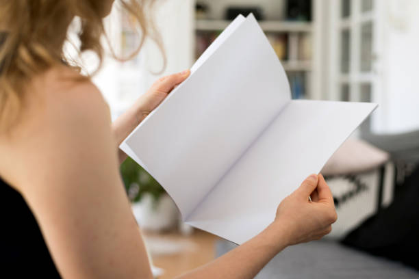 istock Blond young woman is sitting at home holding a blank white brochure with copy space 856003648