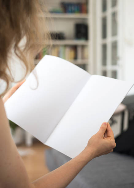 istock Blond young woman is sitting at home holding a blank white brochure with copy space 856003660