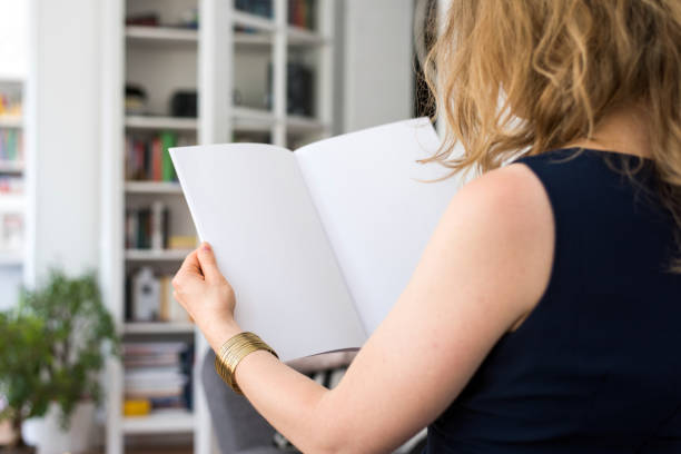 istock Blond young woman is sitting at home holding a blank white brochure with copy space 856003668