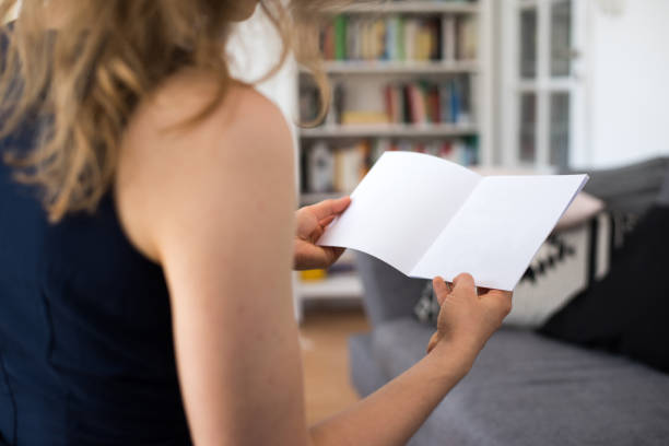 Blond young woman is sitting at home holding a blank white brochure with copy space
