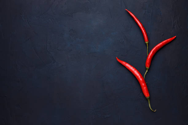 Three red chili peppers on the dark blue stone background. stock photo
