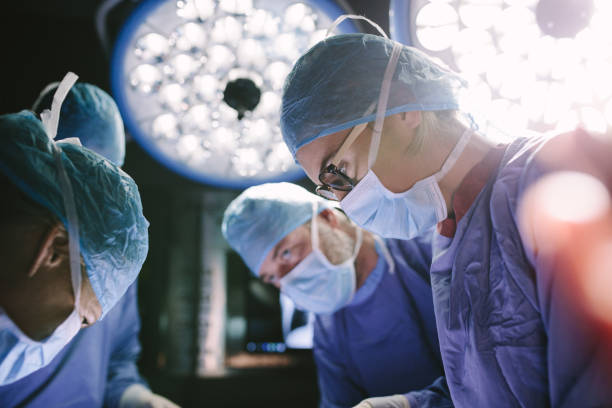 Concentrated surgeon performing surgery with her team Concentrated female surgeon performing surgery with her team in hospital operating room. Medics during surgery in operation theater. medical procedure photos stock pictures, royalty-free photos & images