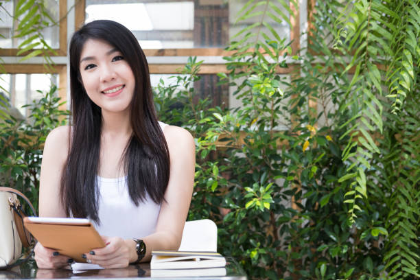 mulher asiática sentar no café ao ar livre. jovem adulto feminino segurar o tablet digital na cafeteria. adolescente feliz sorrir e relaxar em casa. tecnologia, conceito de estilo de vida - retail place attractive female technology contemporary - fotografias e filmes do acervo